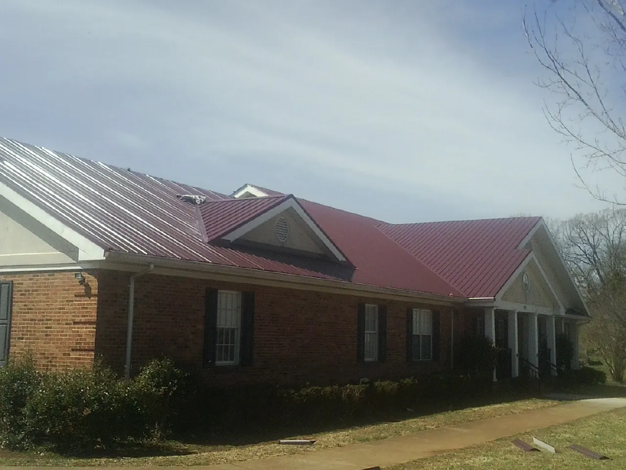 Red metal roof with gabled entries on a long brick building, from a Hail Damage Roof Repair job in Hicksville