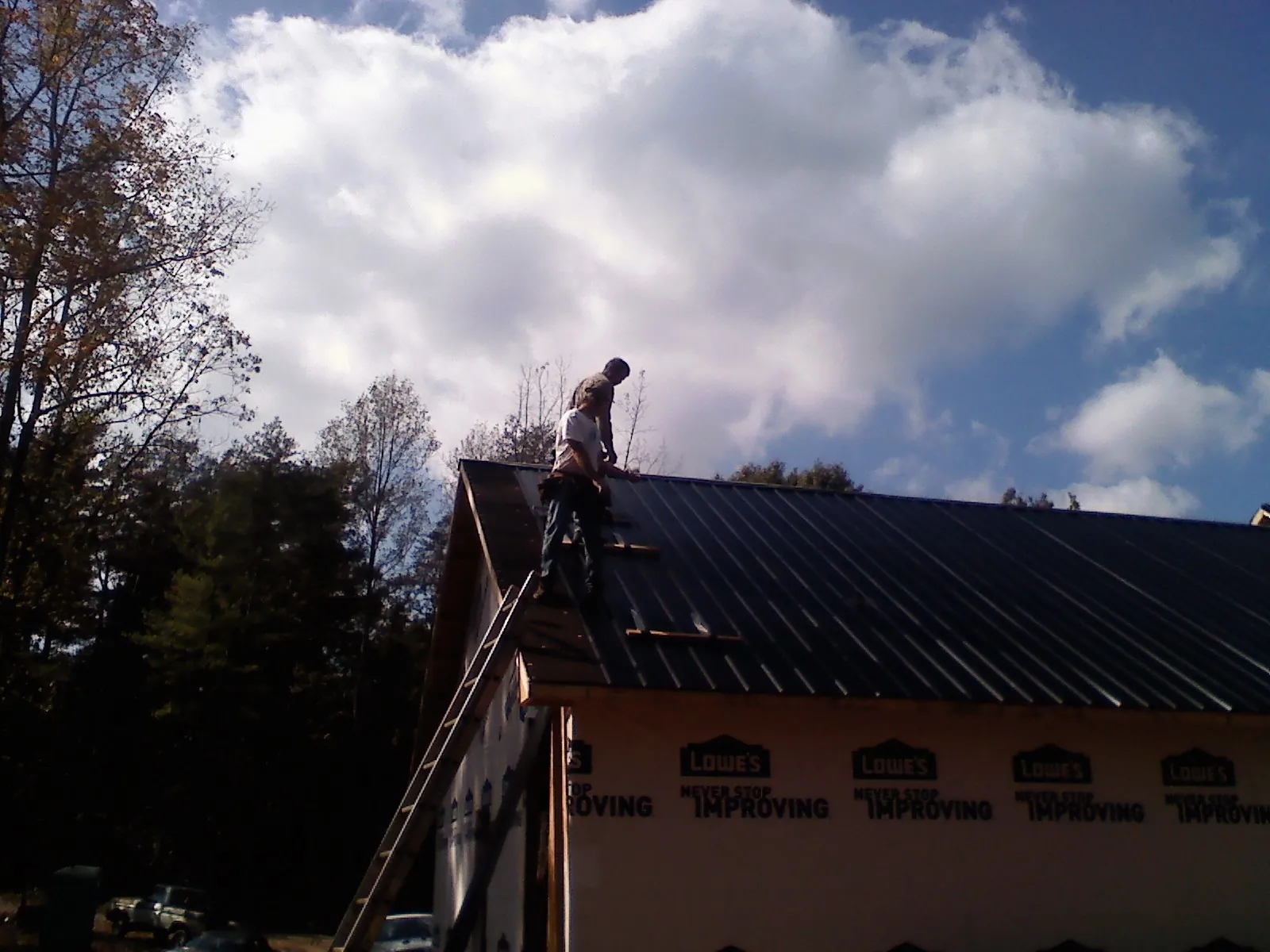 Roofer fastening dark metal panels high against a cloudy sky, from a Roof Inspection job in Hicksville