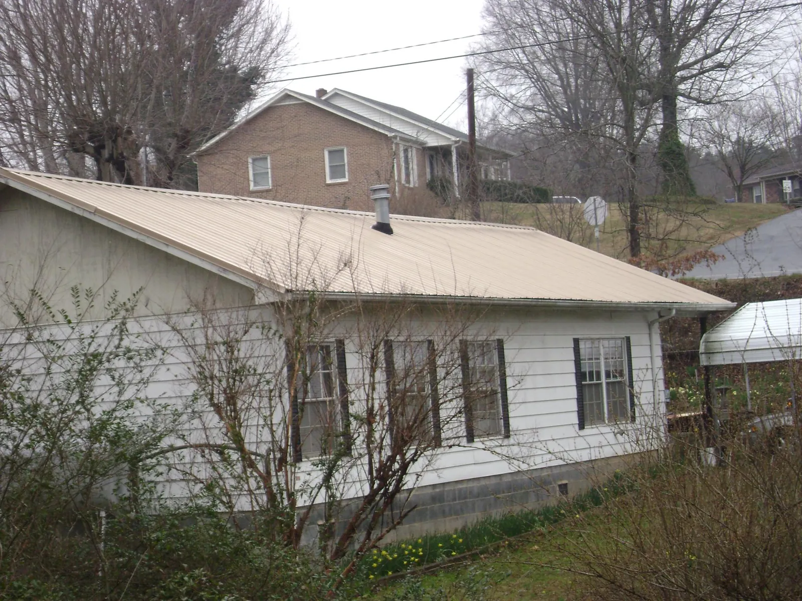 Tan metal roof on a white sided house set into a hillside — Commercial Roofing by Roofing Brothers in Hicksville